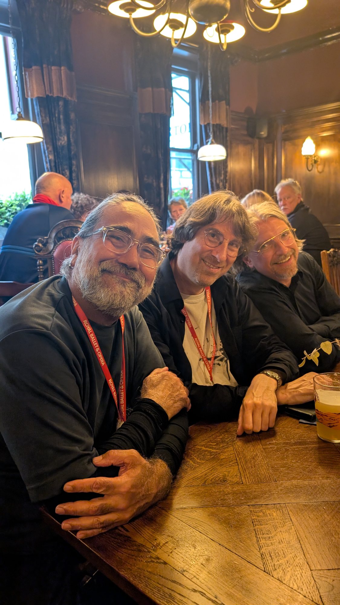 Three people with Royal Ballet and Opera lanyards seated together at a wooden table.