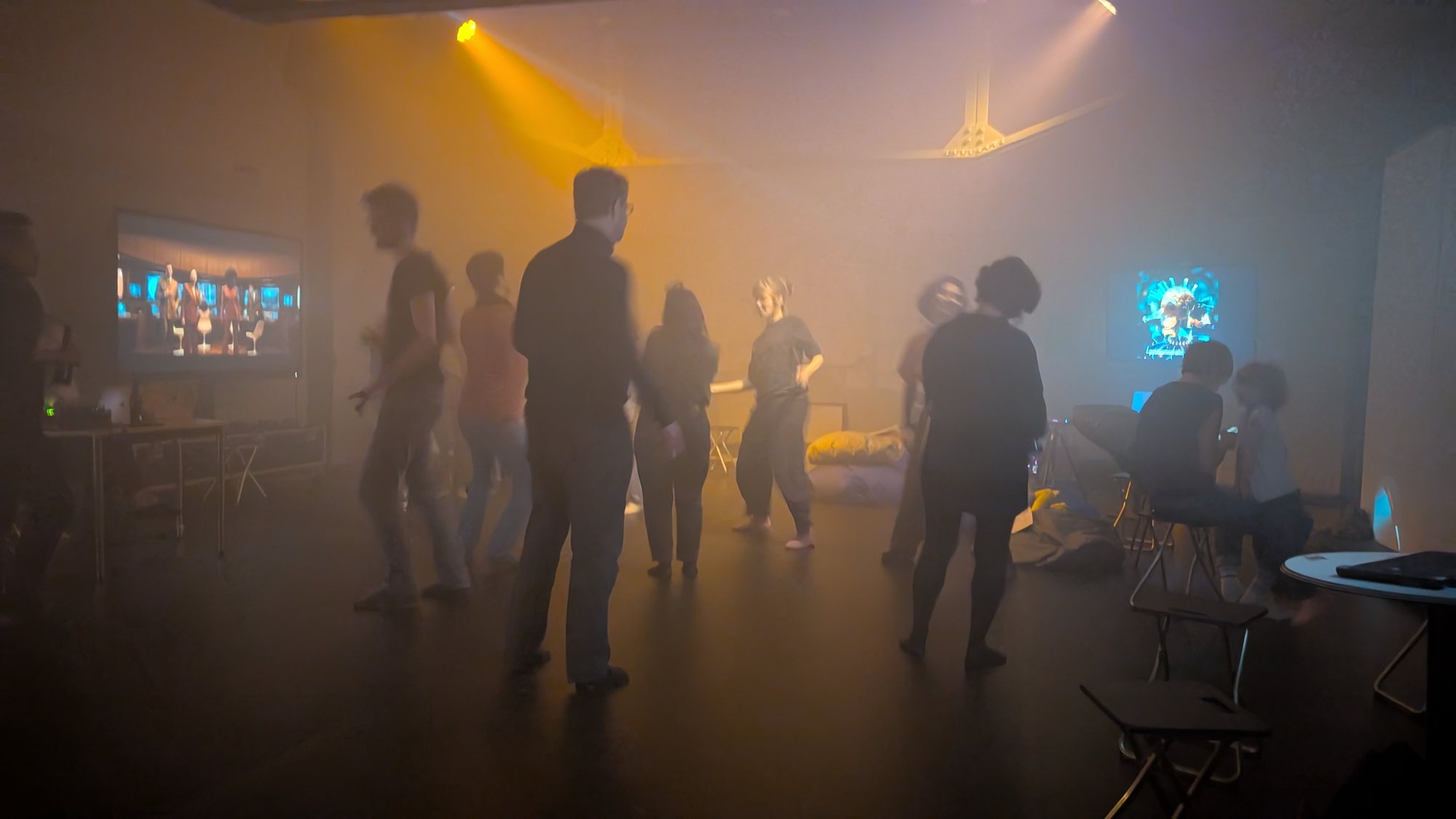 People dancing at night under yellow light, with video projected on the walls.