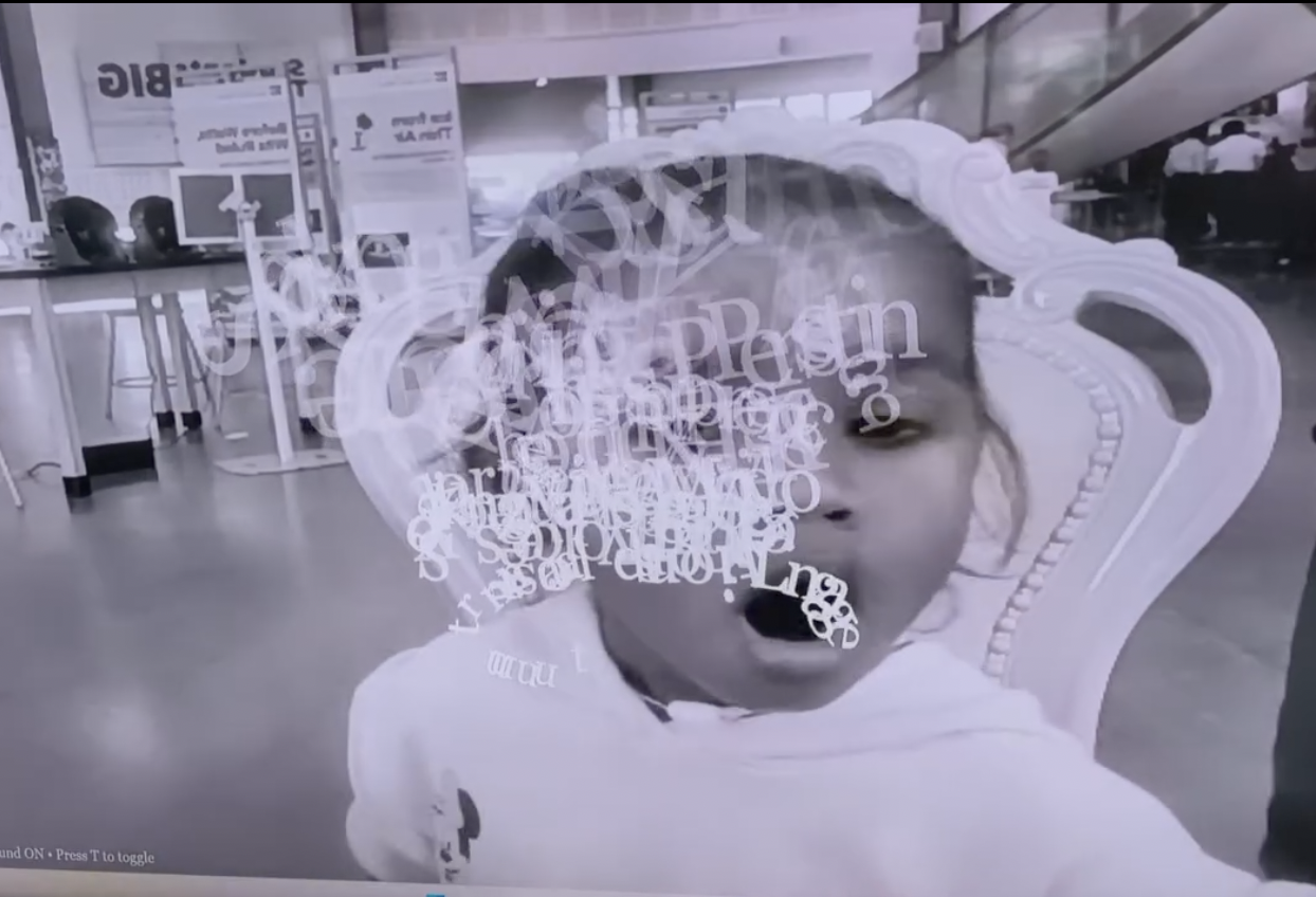 I Am Not Saying: white letterforms drift across a face with an open mouth, seated in a white chair in a room of computers.