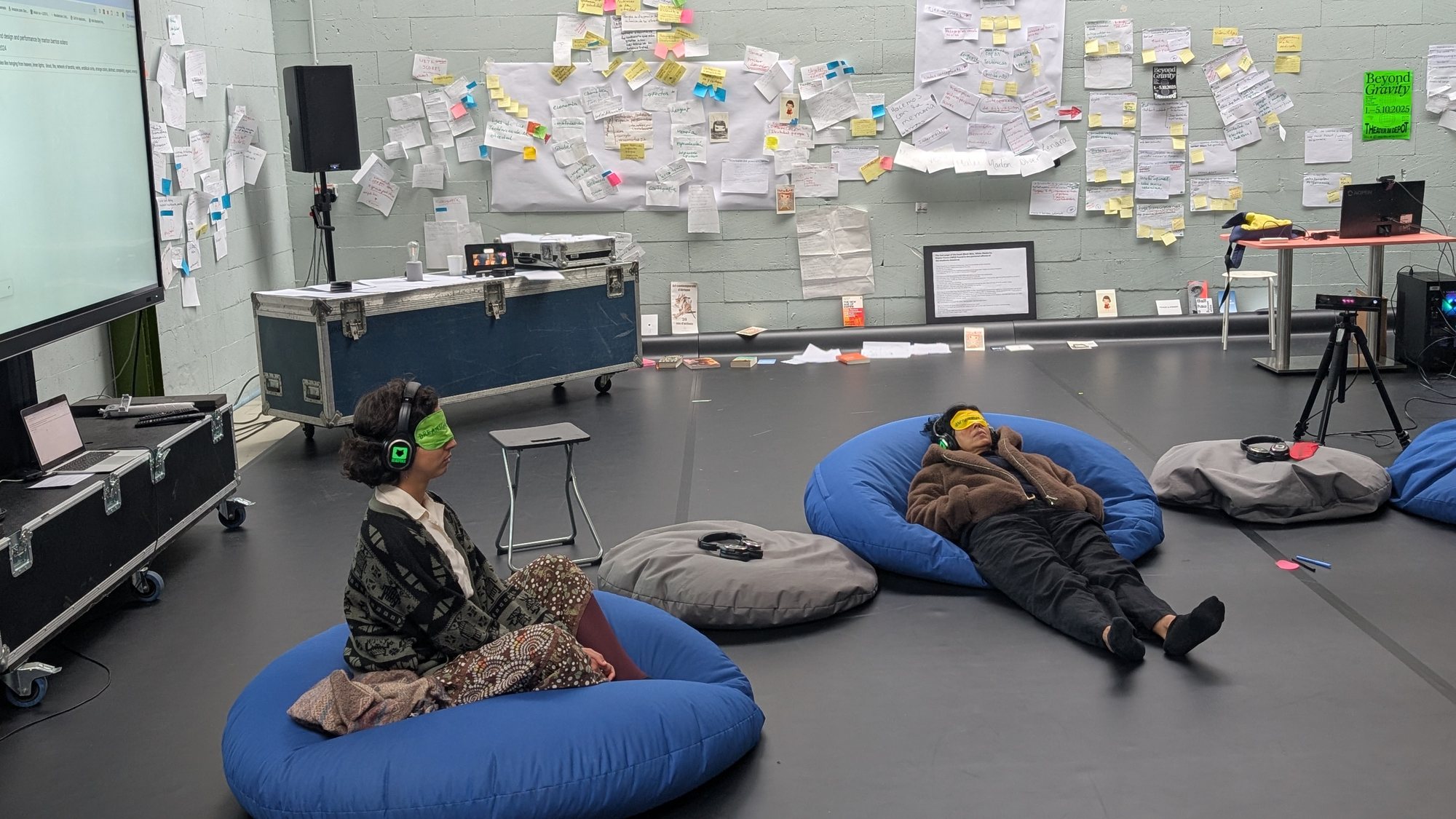 Two people rest on cushions wearing headphones and eye masks, in a studio lined with notes, at Beyond Gravity Festival, 2025.